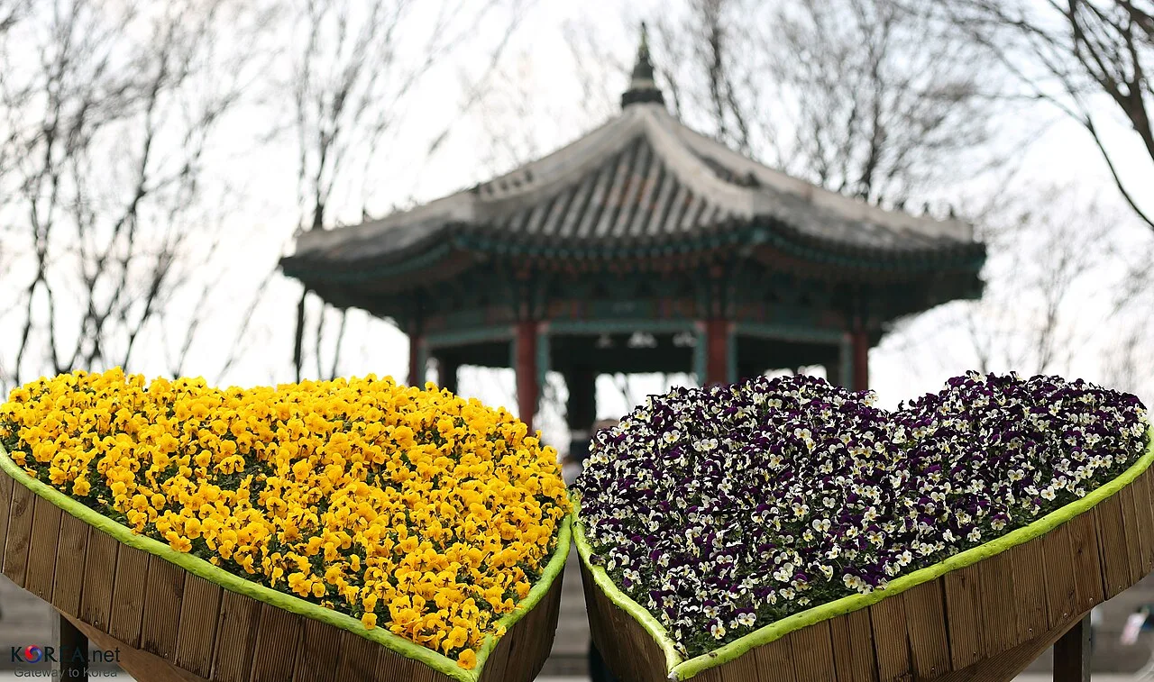 Người mặc áo khoác nâu đi qua hai người khác, xe hơi và người đi bộ đứng dọc theo đường gần các tòa nhà