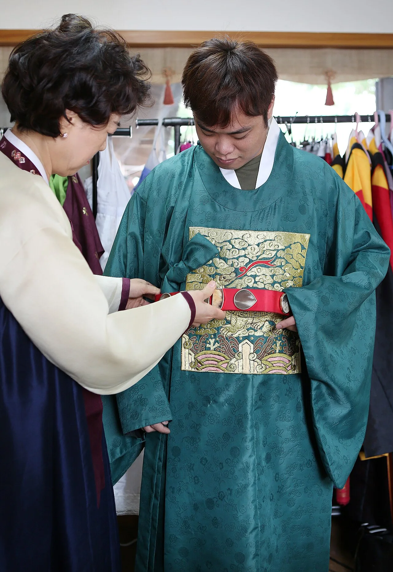 四名穿著韓服的人手持手提包，站在有瓦片屋頂的石牆建築附近。