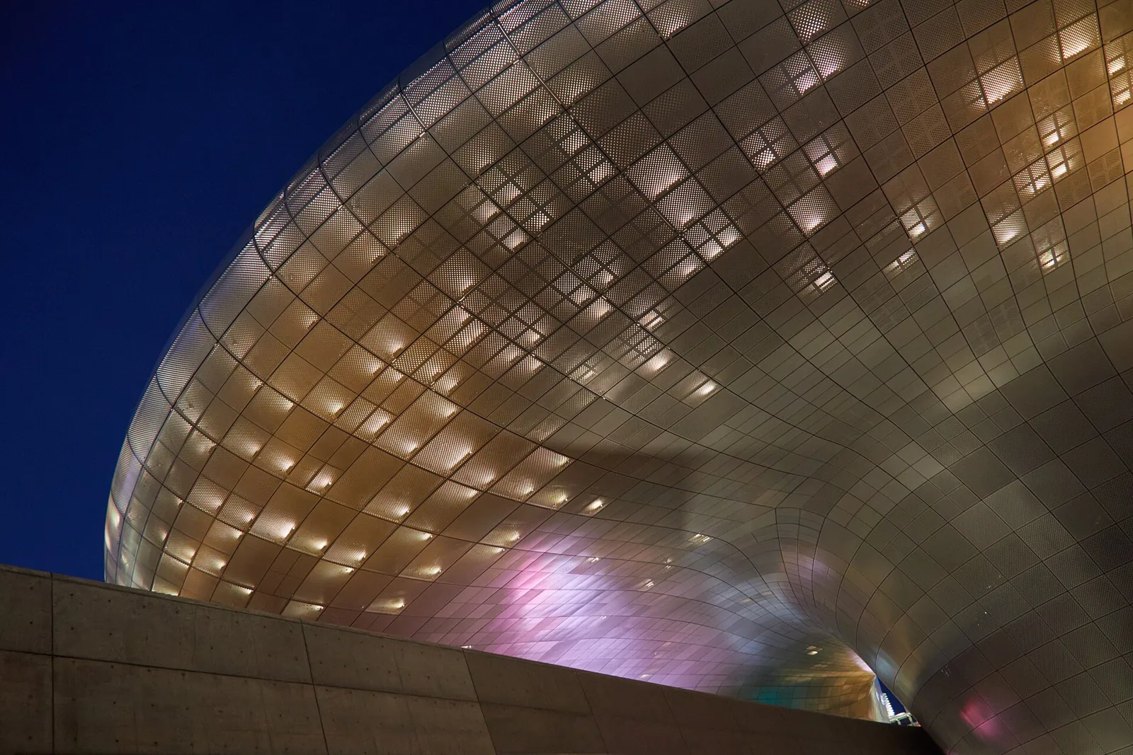 Изогнутый металлический фасад Dongdaemun Design Plaza в вечерней подсветке
