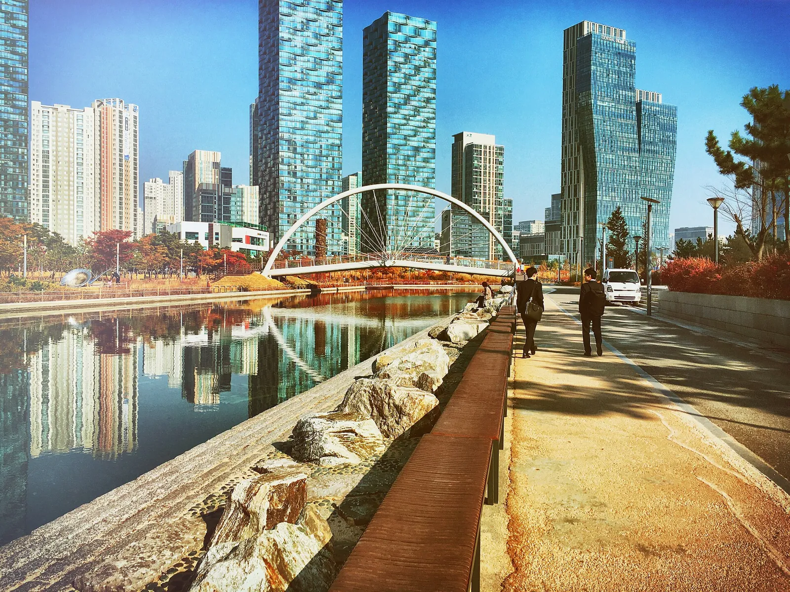 Songdo canal reflecting glass towers and a red footbridge with a few walkers