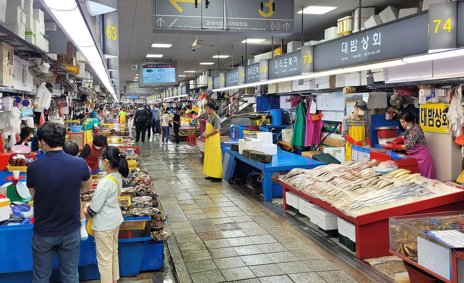 釜山のチャガルチ市場で、魚の屋台が並ぶ屋内の通路を歩く買い物客