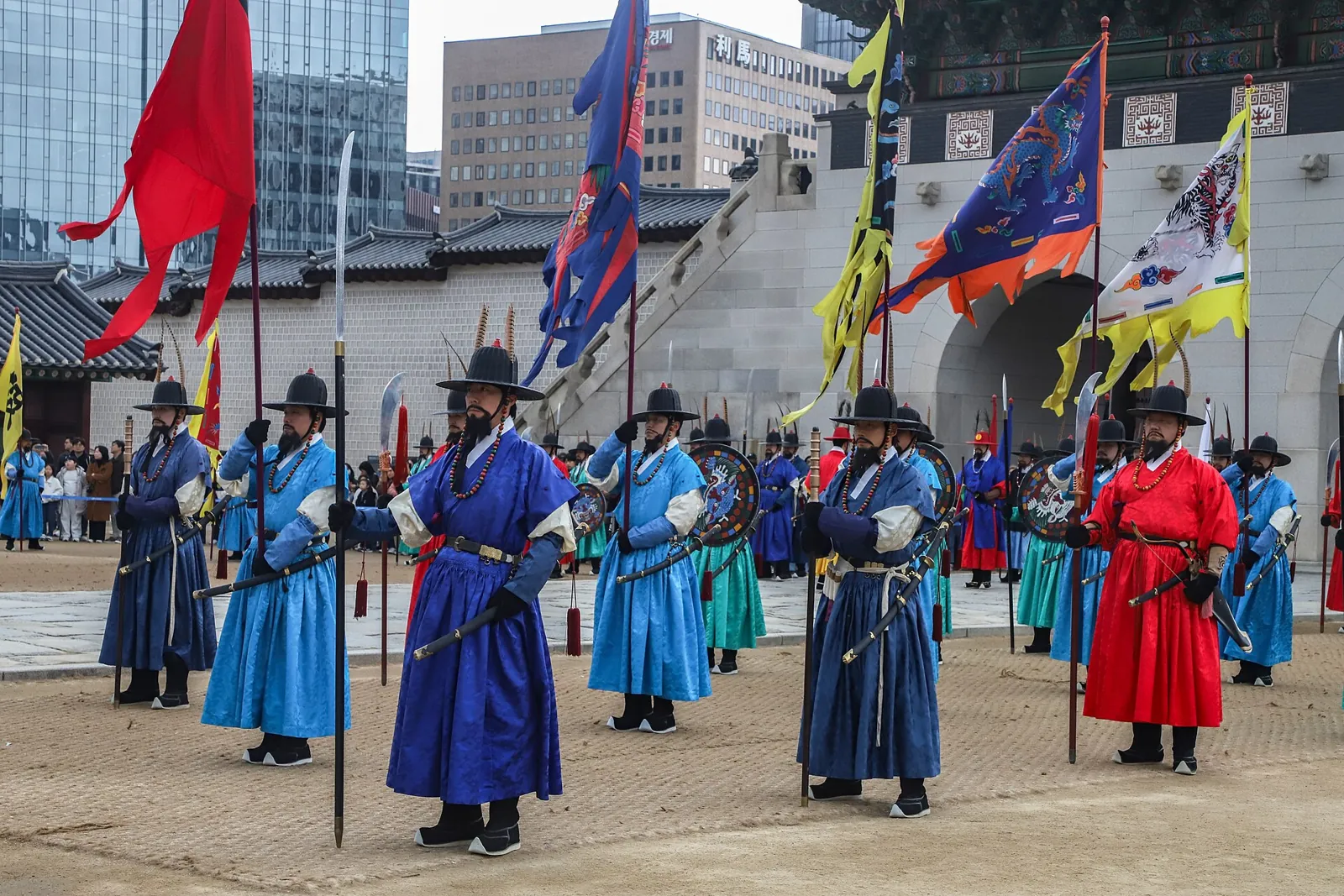 Royal guard ceremony performers in blue and red robes holding flags in front of a palace gate