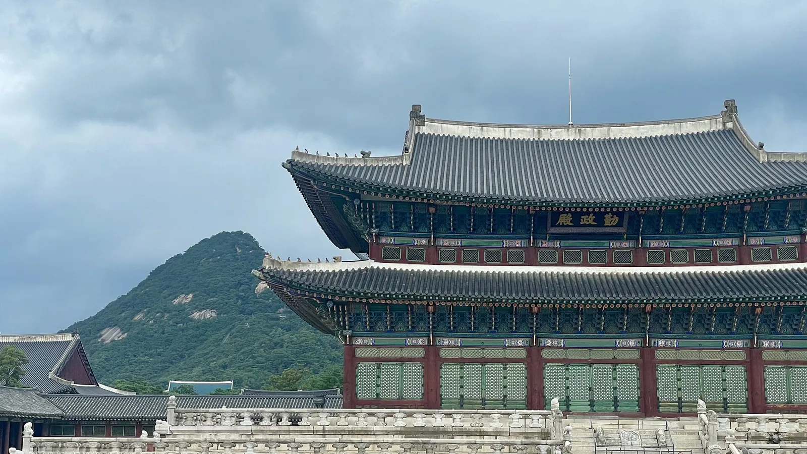 Geunjeongjeon hall at Gyeongbokgung Palace with Bugaksan mountain behind it under a cloudy sky