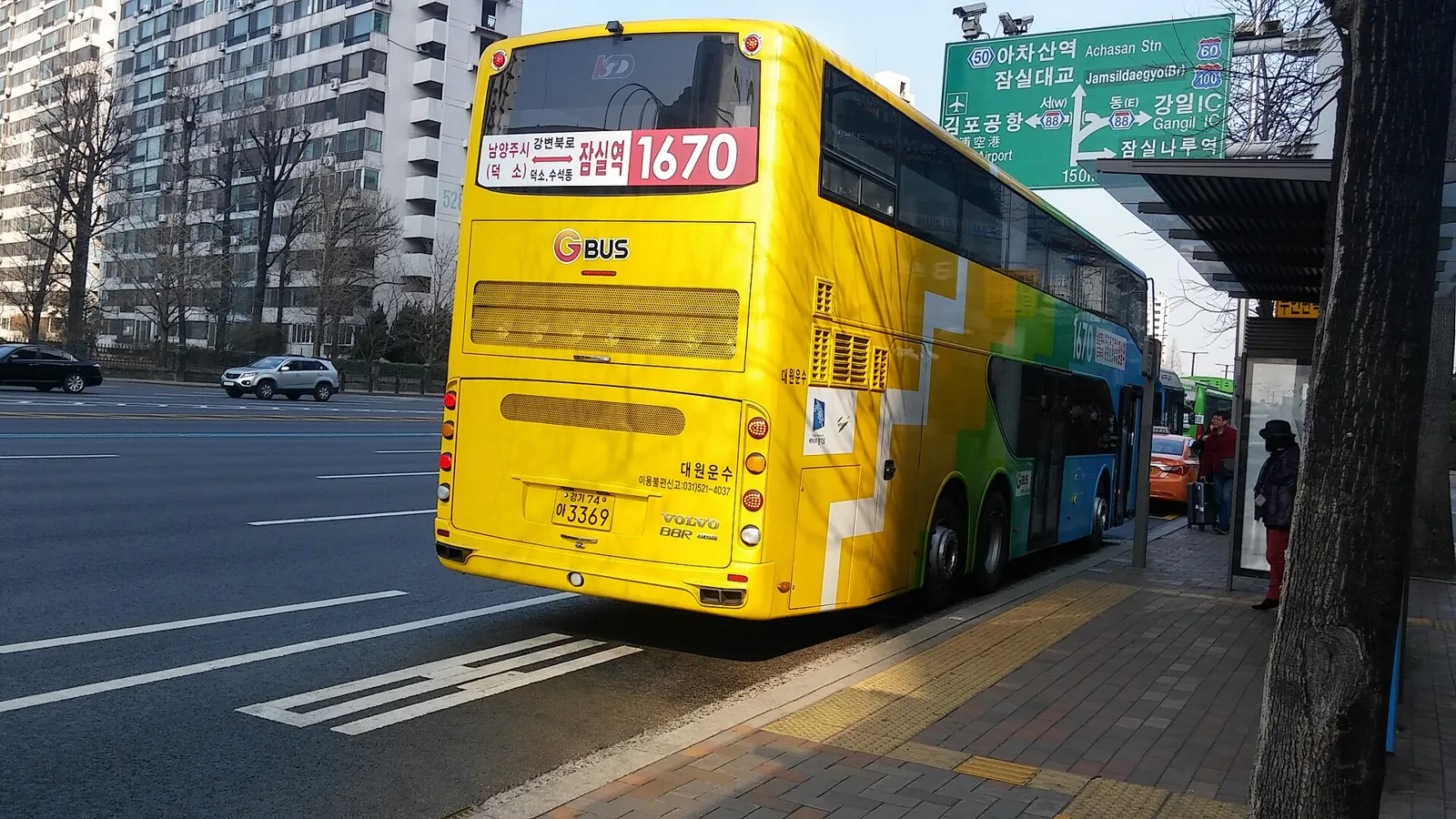 停靠在首爾路邊公車站的黃色雙層巴士,旁邊有乘客候車